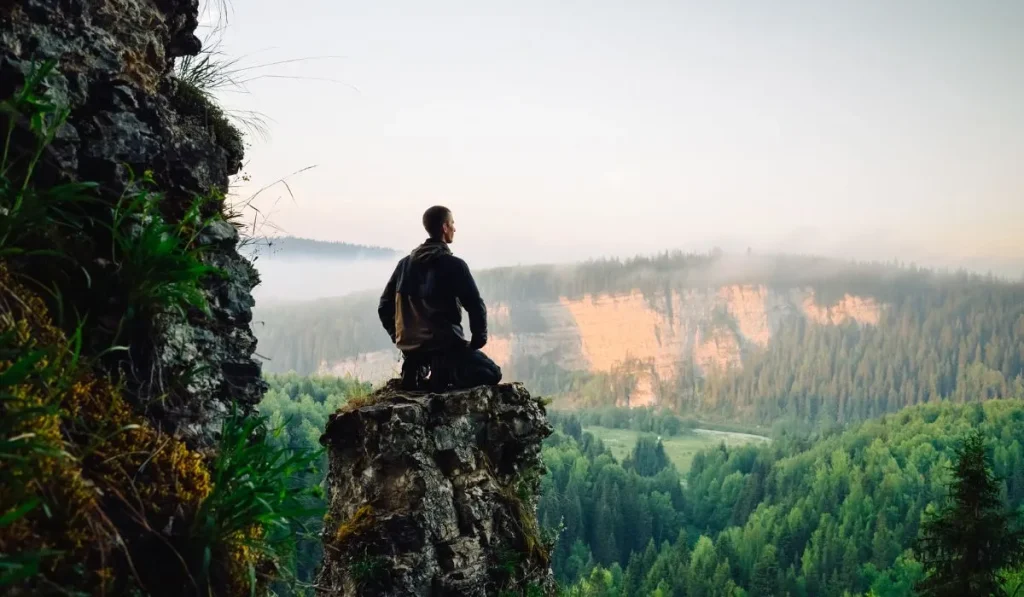 A man sitting on a hill surrounded by nature, looking forward in inner peace.